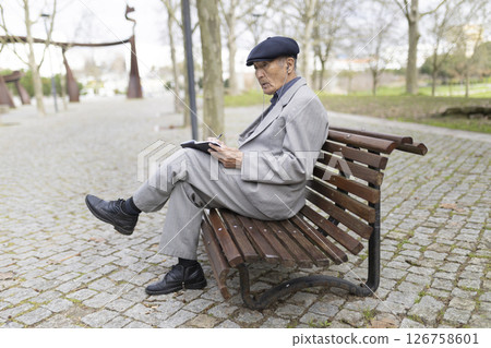 Senior man writing on notebook while listening music on park bench Senior man writing on notebook while listening music on park bench 126758601