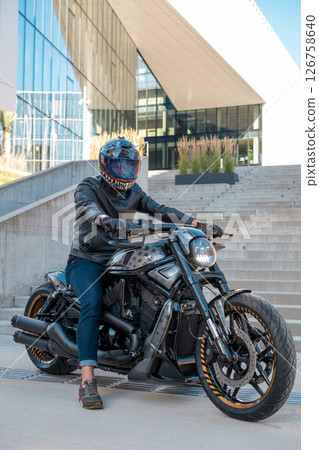 Handsome biker with helmet sitting on his moto against urban backdrop. High quality photo 126758640