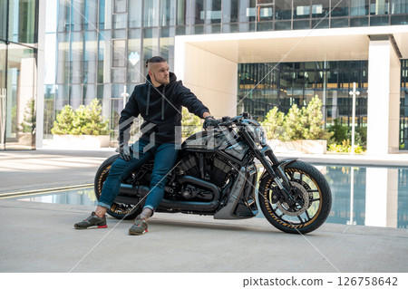 Handsome motorcyclist without helmet sitting on his moto against urban background. High quality photo 126758642
