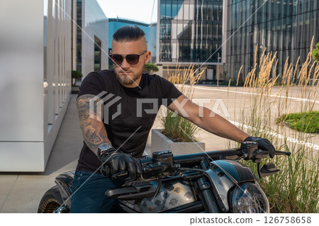 Handsome motorcyclist in sunglasses on his moto against an urban backdrop riding in the city. High quality photo 126758658