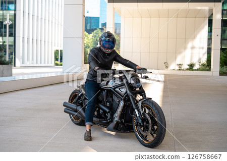 Handsome biker with helmet sitting on his moto against urban backdrop. High quality photo Handsome biker with helmet sitting on his moto against urban backdrop. High quality photo 126758667