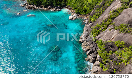 A rocky coastline with striking turquoise water and dense green vegetation on the slopes. Seychelles, Mahe. 126758770