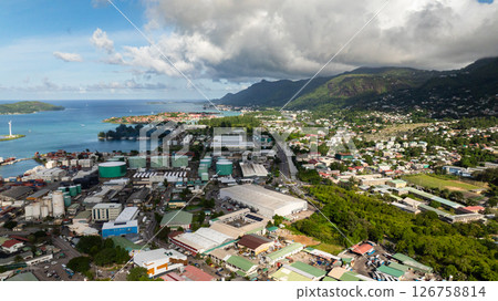 A coastal cityscape with turquoise waters, mountains, and green hills under a partly cloudy sky. Victoria city. Seychelles, Mahe. 126758814