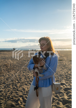 A young woman hugs her Cavalier King Charles Spaniel on the beach at sunset. Warm light, waves, and smiles capture a peaceful, joyful moment of connection and relaxation. A young woman hugs her Cavalier King Charles Spaniel on the beach at sunset. Warm light, waves, and smiles capture a peaceful, joyful moment of connection and relaxation. 126759340