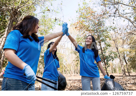 Joyful volunteers celebrating teamwork during a community garbage cleanup in a lush park 126759737