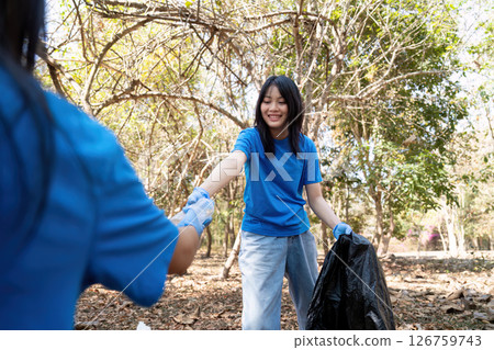 Dedicated volunteer handing over a trash bag during a community cleanup event in a vibrant park 126759743