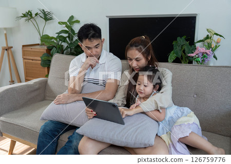 Family enjoying time together on a couch, exploring a tablet with joy and laughter. Family enjoying time together on a couch, exploring a tablet with joy and laughter. 126759776