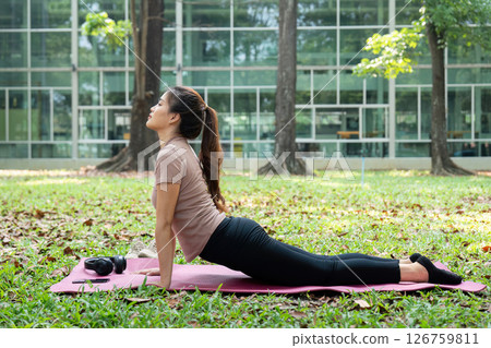 Wellness and Routine. A woman practicing the upward-facing dog pose outdoors, enhancing flexibility and strength. 126759811