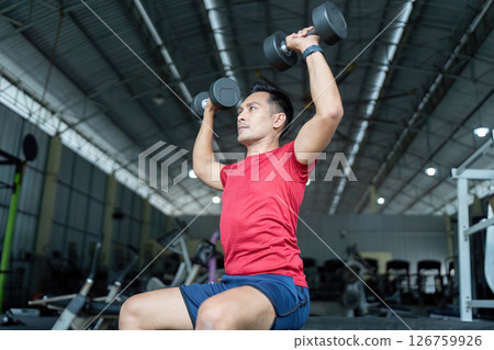 Wellness and Strength Training. Man performing an overhead dumbbell press in the gym. 126759926
