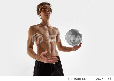 Smiling shirtless volleyball player, with athletic body, gently balances ball in palm while posing confidently against white studio background 126759931