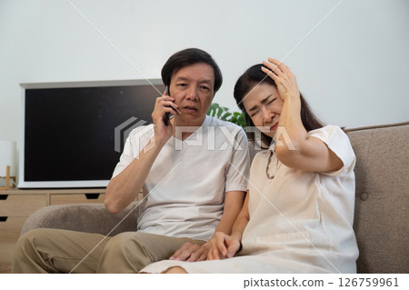 Elderly couple in a moment of concern. A man speaks on the phone while comforting his partner. 126759961