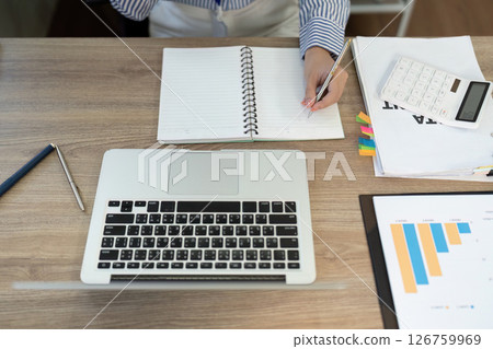 Organized Workspace. Individual writing notes with a laptop and calculator. 126759969