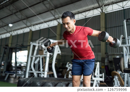 Wellness and Fitness. Man performing dumbbell lateral raises for upper body strength at gym. Wellness and Fitness. Man performing dumbbell lateral raises for upper body strength at gym. 126759996