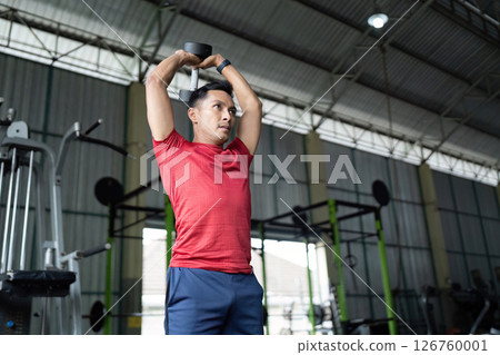 Wellness and Strength. Individual lifting dumbbells overhead in a fitness center. 126760001