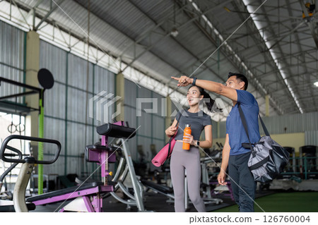 Wellness and Friendship. Friends exploring gym equipment while enjoying fitness journey. 126760004