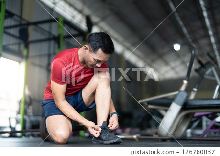 Wellness and Fitness. Man tying shoelaces in gym, preparing for workout. 126760037