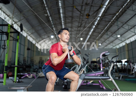 Wellness and Strength. Man performing squat with dumbbell for lower body workout at gym. Wellness and Strength. Man performing squat with dumbbell for lower body workout at gym. 126760060
