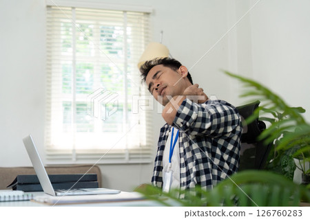 Workplace Wellness. Young man experiencing neck pain while working at a laptop in a home office. 126760283