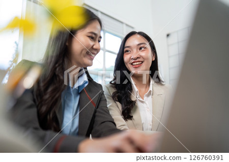 Engaging Discussion. Two businesswomen sharing insights while working on a laptop. 126760391