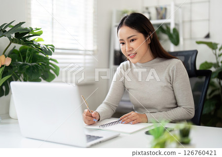 Remote Work and Productivity. Young woman working on laptop in a bright home office. Remote Work and Productivity. Young woman working on laptop in a bright home office. 126760421