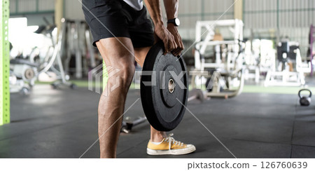 Weightlifting: Young Man Lifting Heavy Plate in Gym Weightlifting: Young Man Lifting Heavy Plate in Gym 126760639