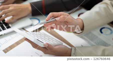 Team Collaboration and Financial Review. Colleagues discussing data with calculator and charts. 126760646