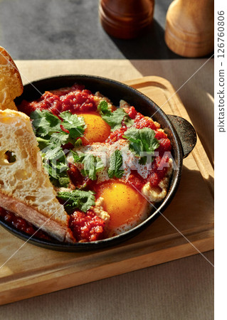 Shakshuka with toasted bread, herbs, and spices in cast iron pan enjoying sunlight 126760806
