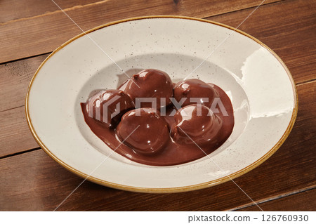 Chocolate profiteroles bathing in a rich chocolate sauce on rustic wooden table 126760930