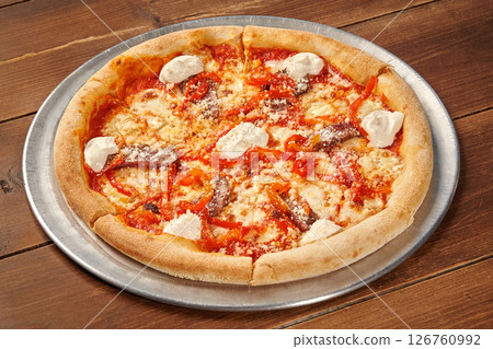 Delicious pizza with anchovies, red peppers, and creamy sauce resting on wooden table 126760992