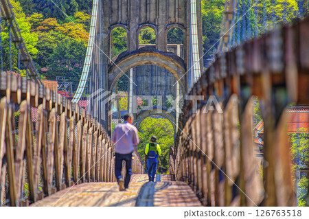 People walking on a suspension bridge surrounded by fresh greenery People walking on a suspension bridge surrounded by fresh greenery 126763518