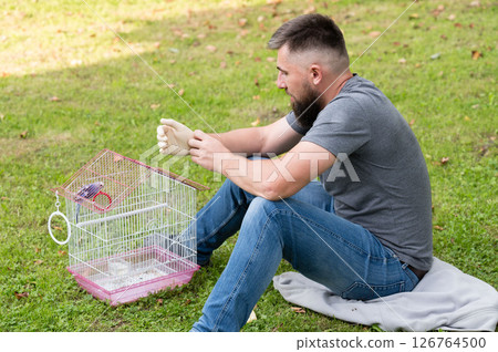 Man gently handles a small bird in its cage outdoors. A peaceful moment of animal care. 126764500