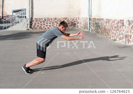 Young man performing a dynamic stretch outdoors, preparing for exercise or a workout. 126764625