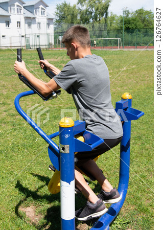 Teenager exercising on outdoor fitness equipment in a park on a sunny day. 126764627
