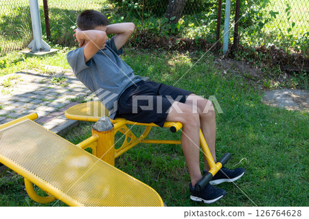 Teenager doing sit-ups on outdoor fitness equipment in a park. 126764628