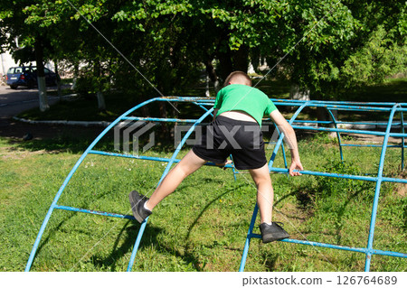 Boy climbing a playground structure outdoors on a sunny day. Active child enjoying playtime. 126764689