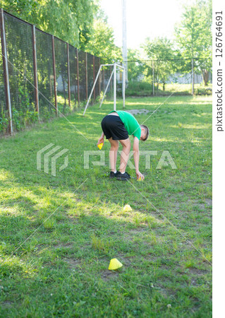Young athlete setting up training cones on a grassy field. Getting ready for practice. 126764691