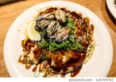 close up of Japanese pan fried Hiroshima Okonomiyaki with seafood and seaweed as toppings, udon noodles at the bottom of the omelette.  126764783