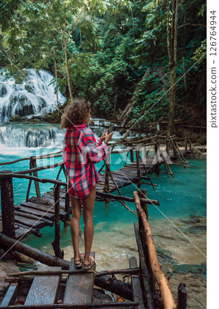 Traveller woman take pictures on phone on bridge at cascade waterfall in Luwuk, Sulawesi, Indonesia 126764944