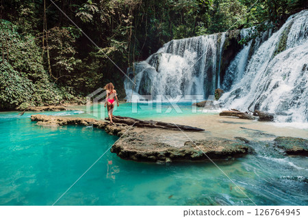 Woman in swimsuit on rock at scenic cascade waterfalls with turquoise water 126764945