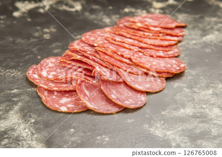Sliced cured meat arranged on a dark surface 126765008