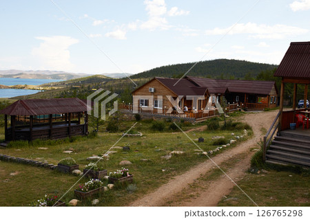 Wooden houses in a rustic style stand in a picturesque place against the backdrop of hills and trees Wooden houses in a rustic style stand in a picturesque place against the backdrop of hills and trees 126765298
