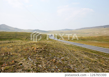 The long highway stretches through vast meadows under a clear sky. 126765300