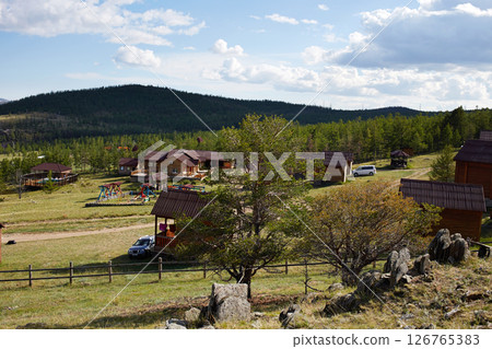 A tourist center with wooden houses in a rustic style against the backdrop of hills and trees. 126765383