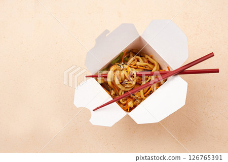 Noodles served in a white takeout box with chopsticks on a simple background 126765391