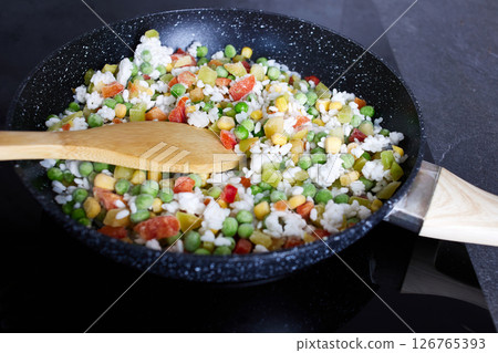 Fresh vegetables with rice, including peas, corn and sweet peppers, are fried in a frying pan. Fresh vegetables with rice, including peas, corn and sweet peppers, are fried in a frying pan. 126765393