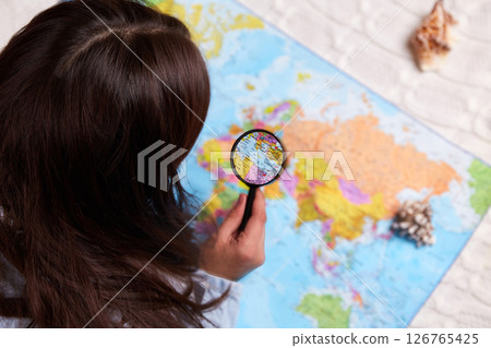 The girl explores the world map with a magnifying glass The girl explores the world map with a magnifying glass 126765425