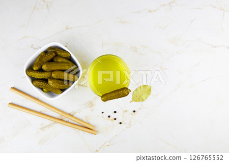 Pickled cucumbers in a bowl and pickle juice in glass on a light background. 126765552