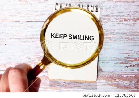 KEEP SMILING words cognized with a magnifying glass in a blank notebook KEEP SMILING words cognized with a magnifying glass in a blank notebook 126766565