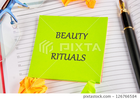 A bright green notepad with the words beauty rituals sits on an organized desk surrounded by colorful sticky notes, glasses, and a pen, highlighting a focus on personal care practices 126766584