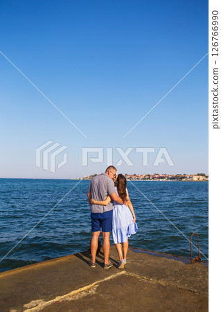 Young happy couple at the seaside stands with their backs to the camera Young happy couple at the seaside stands with their backs to the camera 126766990